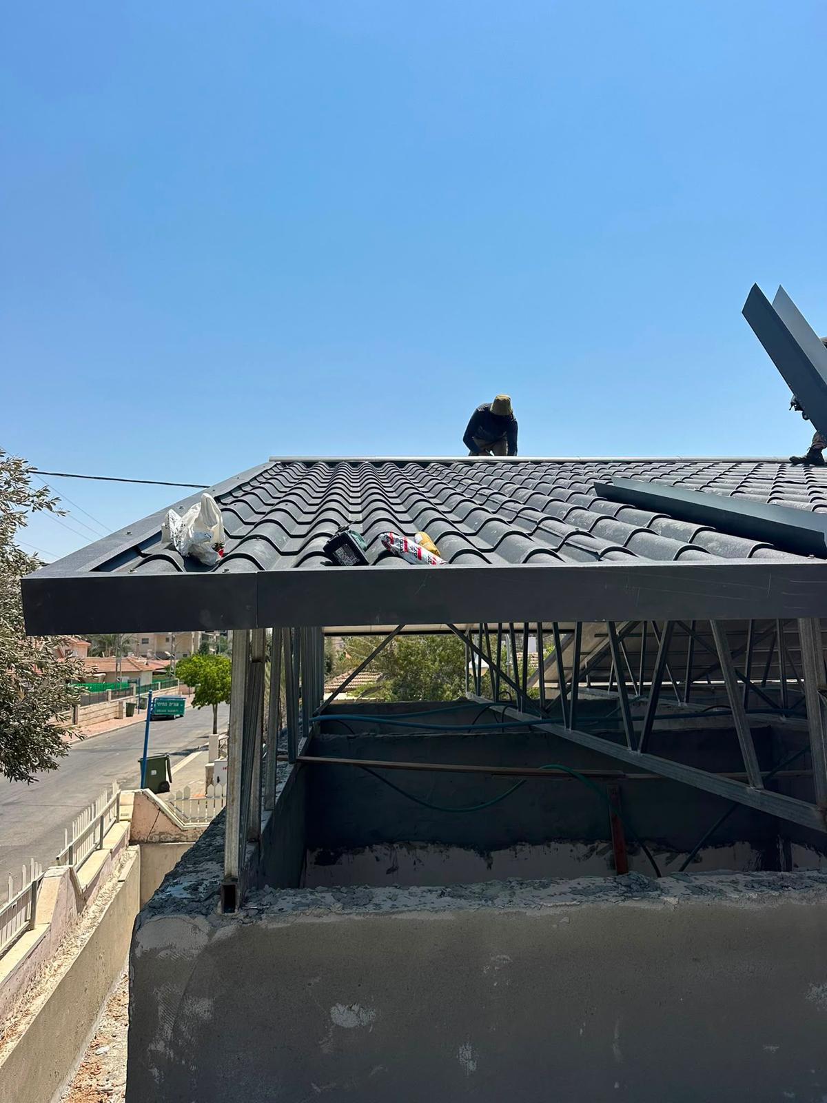 עובד מרכיב גג בדמוי רעפים שחור על קונסטרוקציית פלדה בבית פרטי